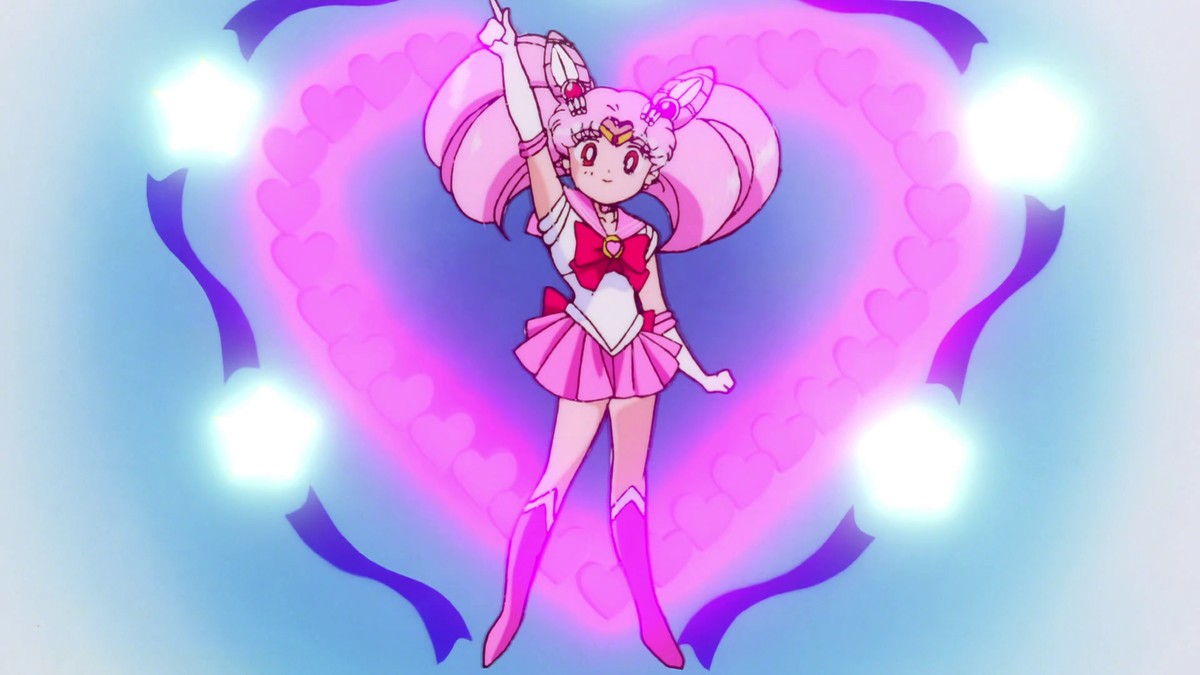 Sailor Chibi Moon landing the final pose of her transformation, one arm raised, a heart of pink hearts blooming behind her.