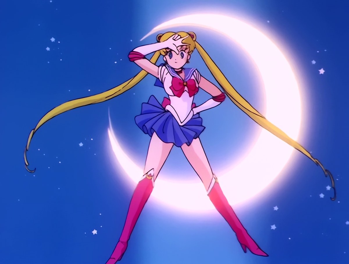 Sailor Moon landing the final pose of her transformation, one hand at her brow and the crescent moon burning white behind her