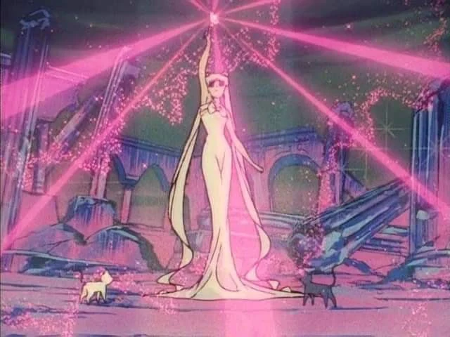 Queen Serenity in a white gown standing among the broken columns of the Moon palace with one arm raised to the sky, pink beams of light streaming out from her hand, and Artemis and Luna at her feet