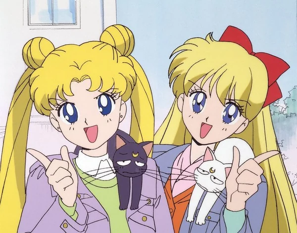 Usagi and Minako side by side in jackets, smiling and pointing, with Luna perched on Usagi&rsquo;s shoulder and Artemis on Minako&rsquo;s