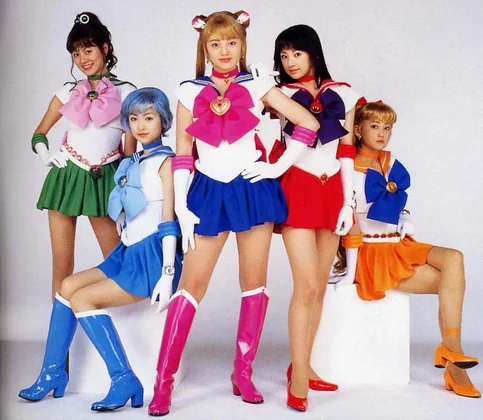 The five live-action guardians in costume against a white backdrop: Jupiter, Mercury, Moon, Mars and Venus, with Venus perched on a block