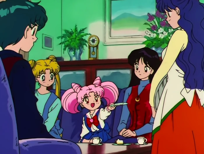 Chibiusa sitting on a sofa in the middle of the group, talking with one hand out, teacups on the table in front of her and every one of them turned toward her