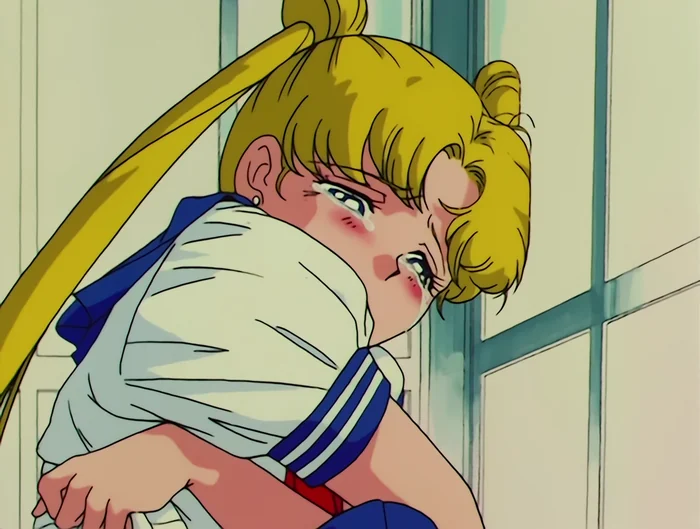 Usagi crouched down against a classroom door with her arms round her knees, face turned away, crying