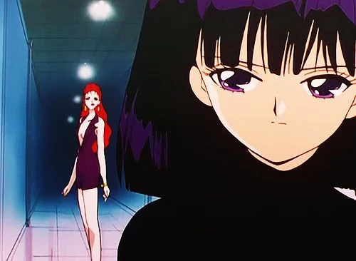 Hotaru&rsquo;s face large in the foreground, turned to one side, while a tall red-haired woman in a short dark dress walks down a lit corridor behind her
