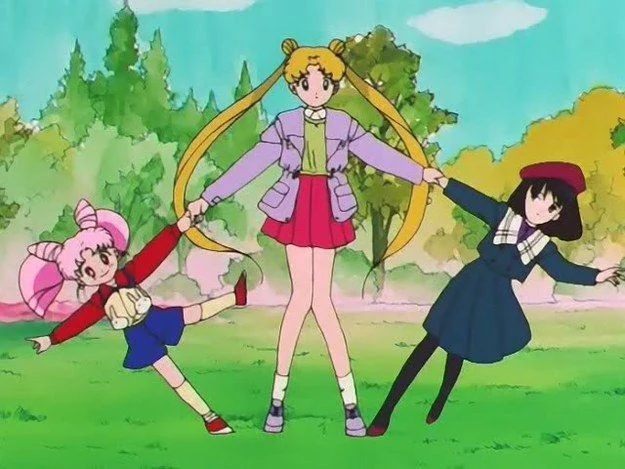 Usagi, Chibiusa and Hotaru holding hands in a ring on the grass in a park, leaning back and spinning, trees and a blue sky behind them