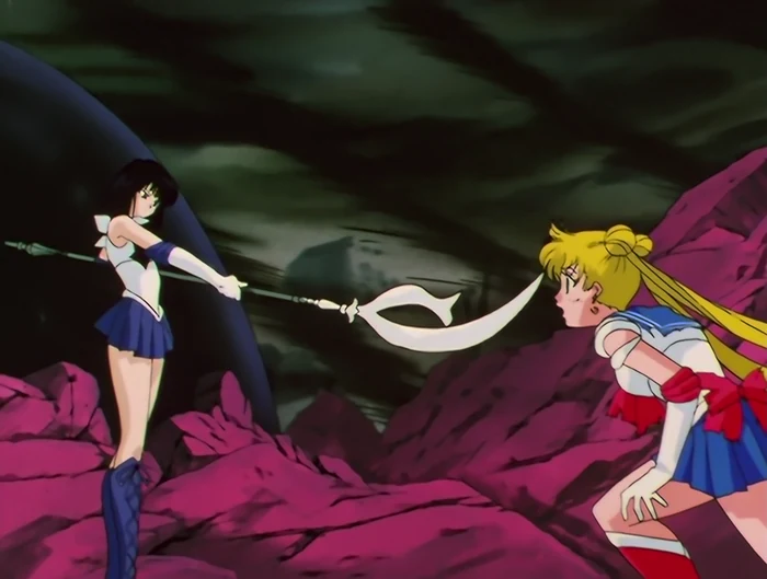Sailor Saturn standing on dark red rock holding the glaive out level, its blade close to Sailor Moon, who is bent forward facing her under a black sky