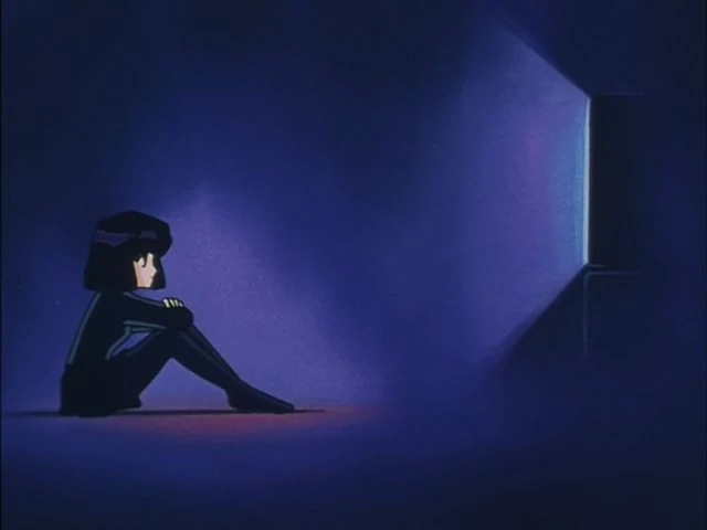 Hotaru sitting on the floor of a dark room with her arms round her knees, a single lit window across the room from her