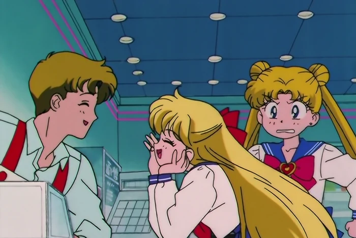 Minako leaning on a shop counter with her chin in her hands, beaming up at the boy behind the register, while Usagi stands behind her looking thoroughly unimpressed