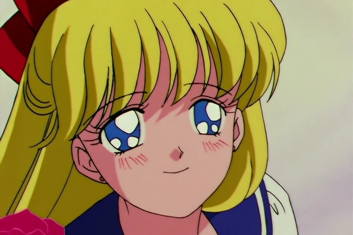 a close-up of Minako looking up with her chin tilted, wide blue eyes and a small pleased smile, a red bow behind her and a pink rose at her shoulder