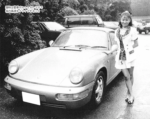 Black and white magazine photo of Naoko Takeuchi standing beside a Porsche, with a printed Japanese caption