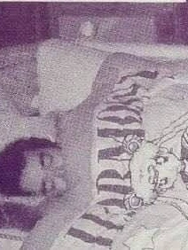 A grainy magazine photo of a dark-haired man asleep on his side under a Sailor Moon blanket printed with Usagi and a banner of lettering