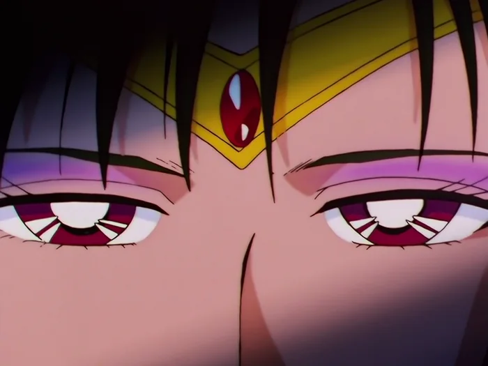 An extreme close-up of Sailor Pluto’s eyes under her gold tiara and its red stone, the lids heavy and the stare fixed